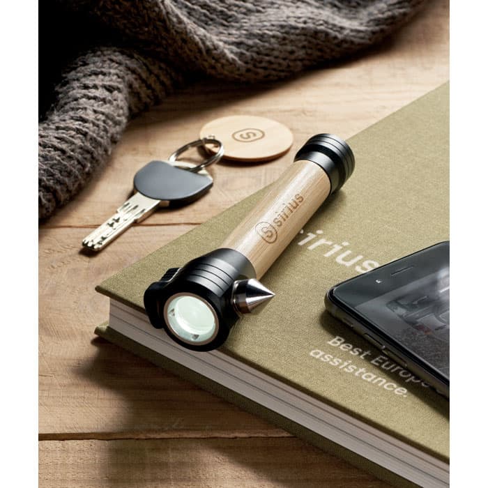 A flashlight with a wooden body and black ends rests on a green book beside a key, a phone, and a knit item.