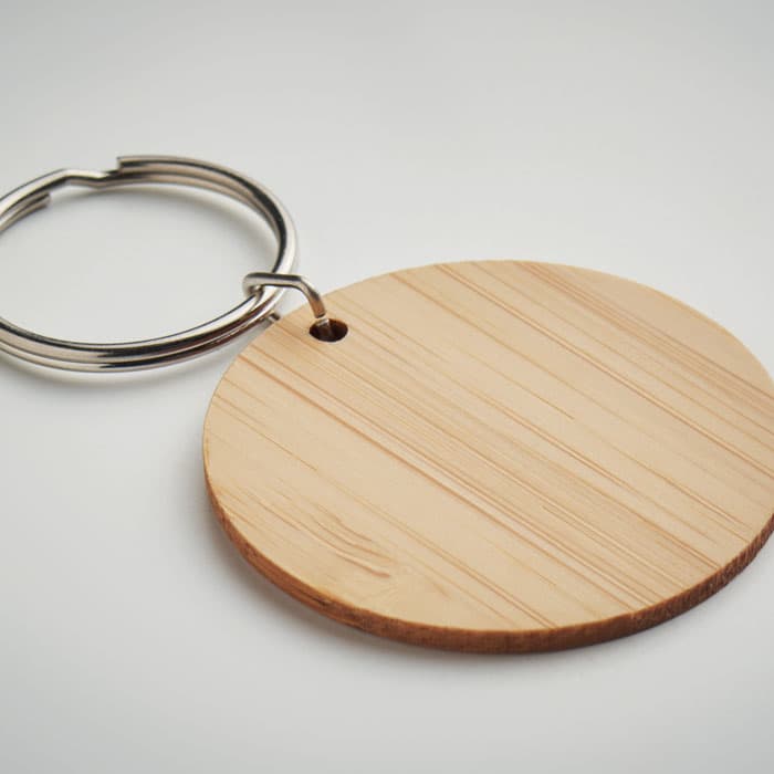 A keychain featuring a circular wooden disc with a smooth texture and a metal ring. The wood is light in colour.