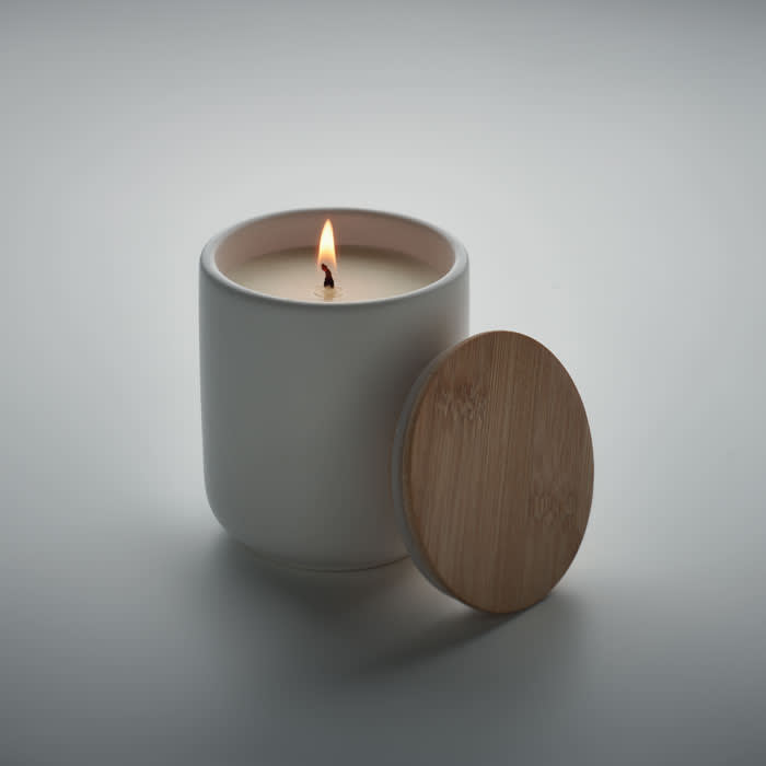 A candle in a white container with a wooden lid, featuring a lit wick. The setting is minimalistic and serene.