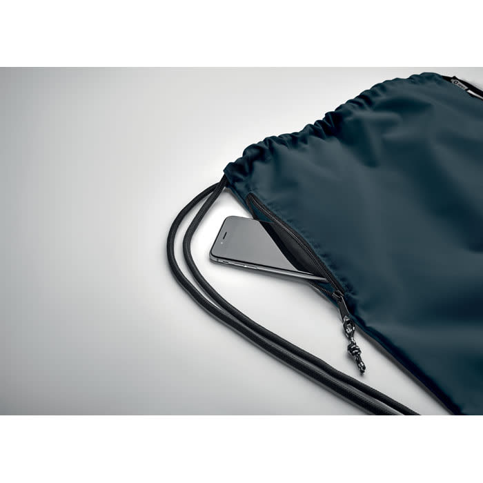A drawstring backpack in dark blue with a phone visible in the zippered compartment.
