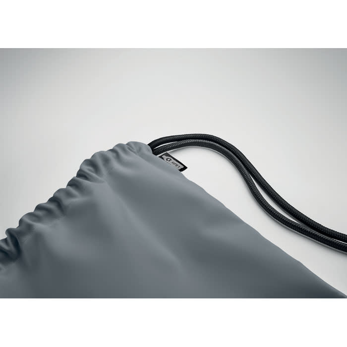 A drawstring bag in a muted grey colour with a textured finish and a black cord. It features a logo on the side.