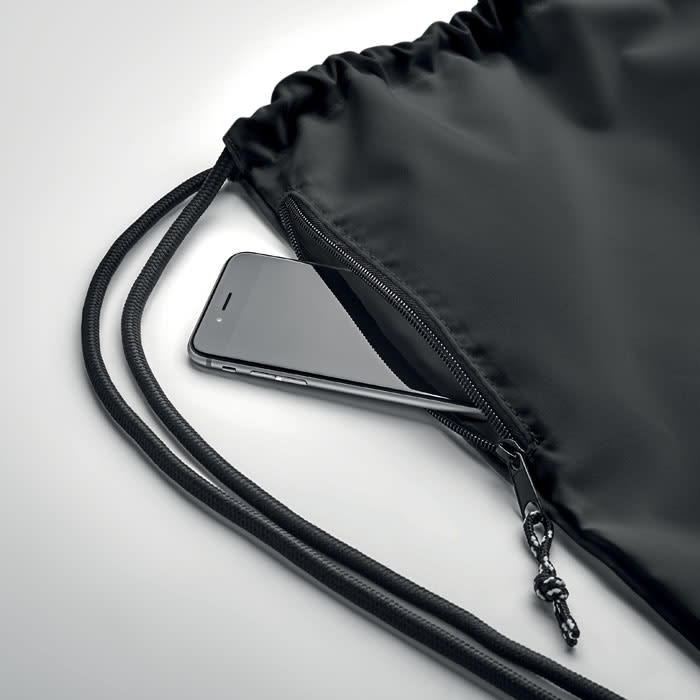 A black drawstring bag with a phone partially visible in the zipper pocket. The bag has a logo.