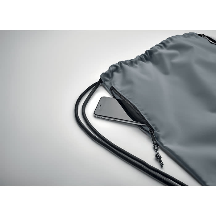 A grey drawstring bag with a smartphone partially visible inside the zippered pocket. The bag has black cords.