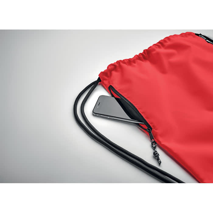 A red drawstring bag with black cords, featuring a smartphone partially visible in its side pocket.