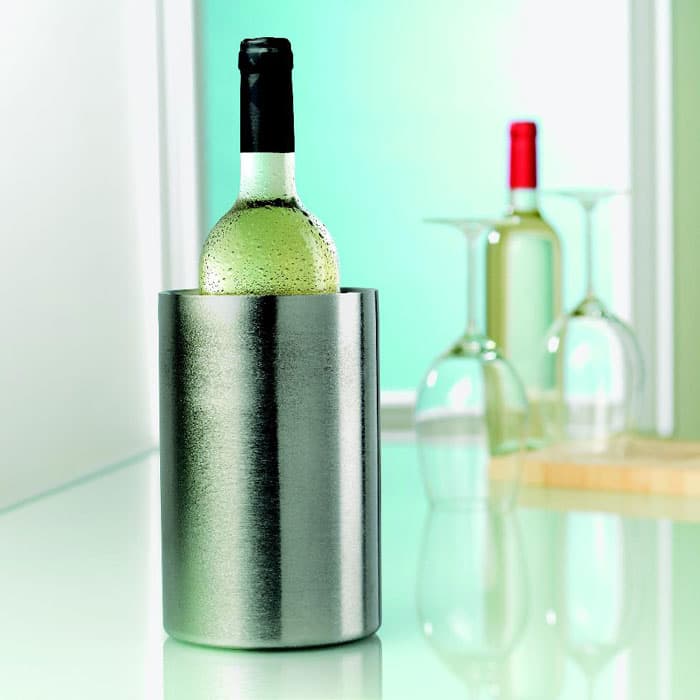A drink bottle cooler in stainless steel, holding a bottle of white wine, with a blurred background of glasses and a red bottle.
