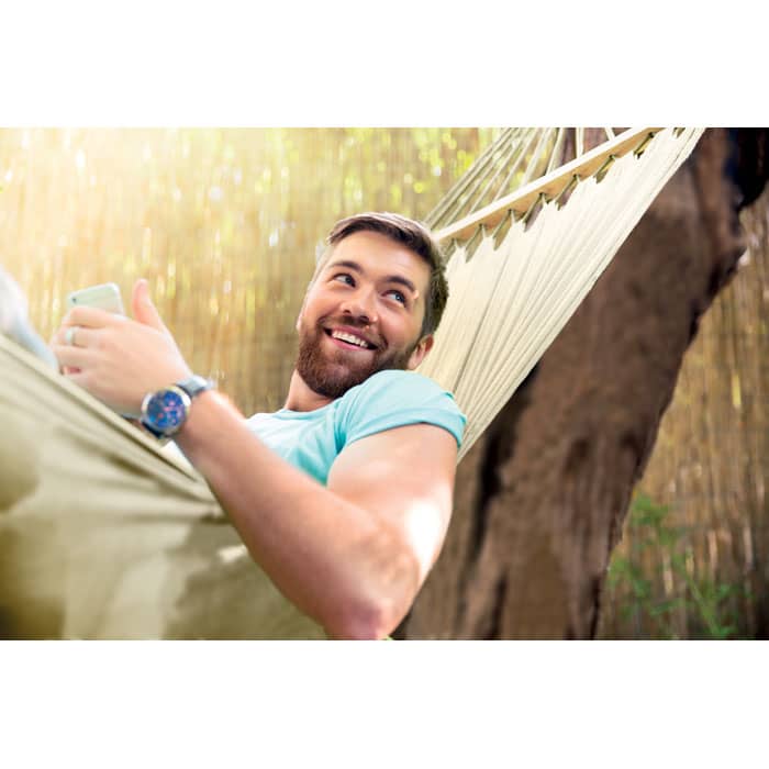A man with a beard relaxes in a light-coloured hammock, smiling and enjoying his surroundings.