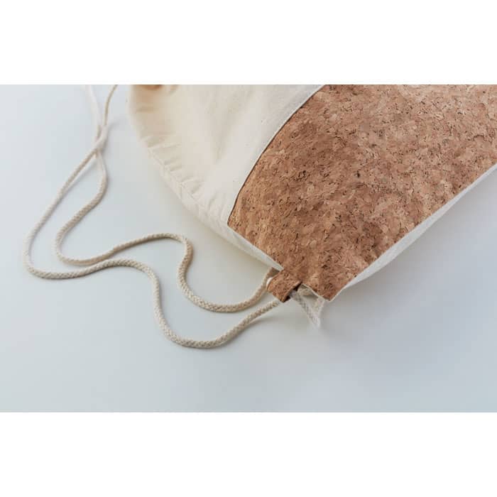 A drawstring bag in natural fabric with a cork accent and beige drawstrings. Features a logo on the front.