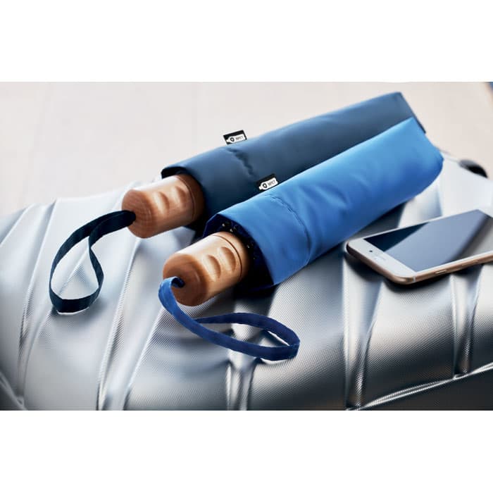 A drink bottle and an umbrella in blue and navy, with a wooden handle, resting on a silver surface beside a smartphone.