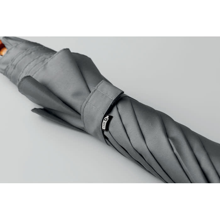 A grey umbrella with a tied strap and a small branding logo on the handle.