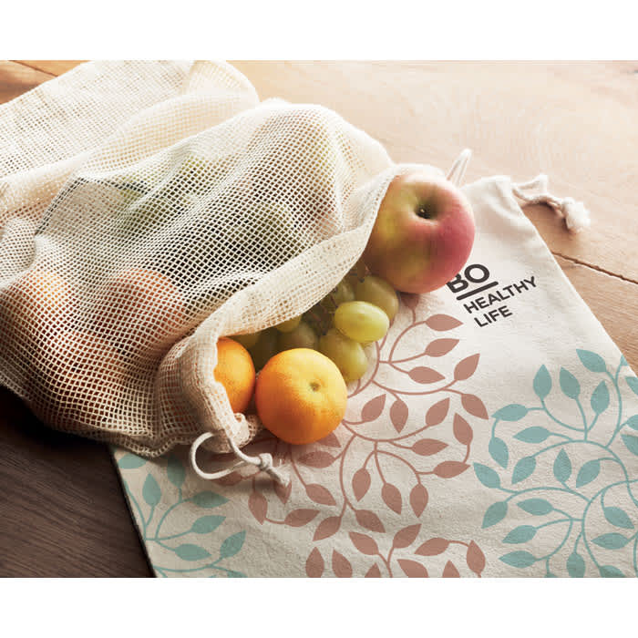 A mesh produce bag with fruits, including apples and grapes, featuring a decorative leaf pattern in pastel colours.