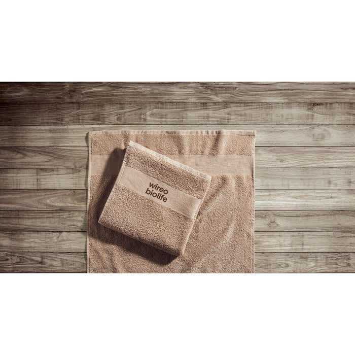 A set of beige towels featuring a folded towel on top of a larger one, both displayed on a wooden surface.