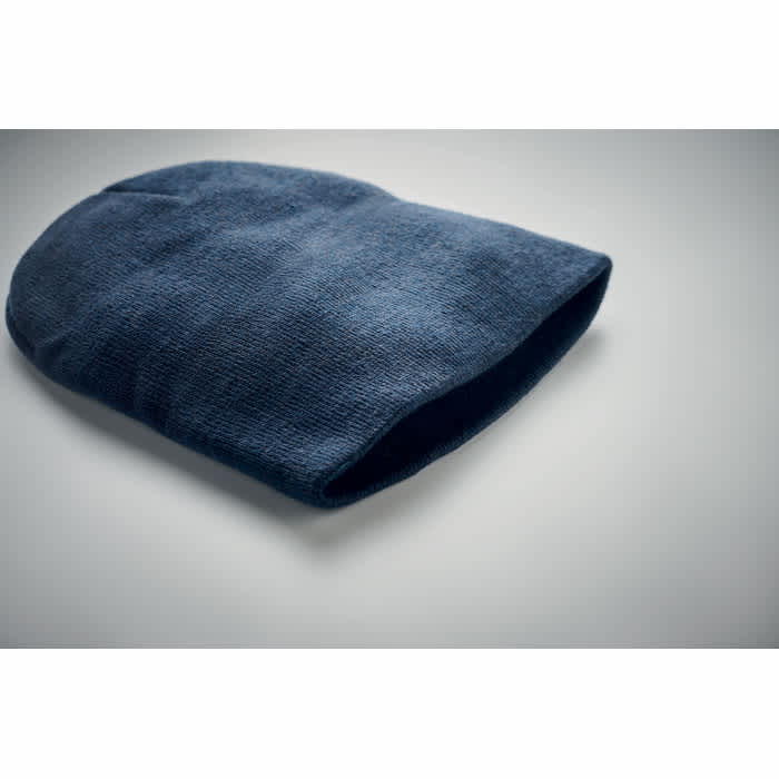 A dark blue beanie hat laid flat on a plain surface, featuring a textured fabric. The item has no visible branding.