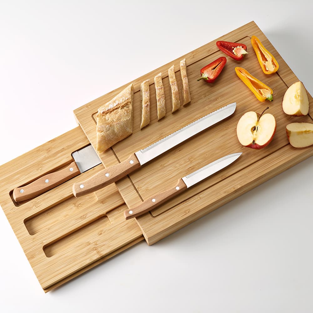 A bamboo cutting board with two kitchen knives, slices of bread, apple, and assorted colourful vegetables.