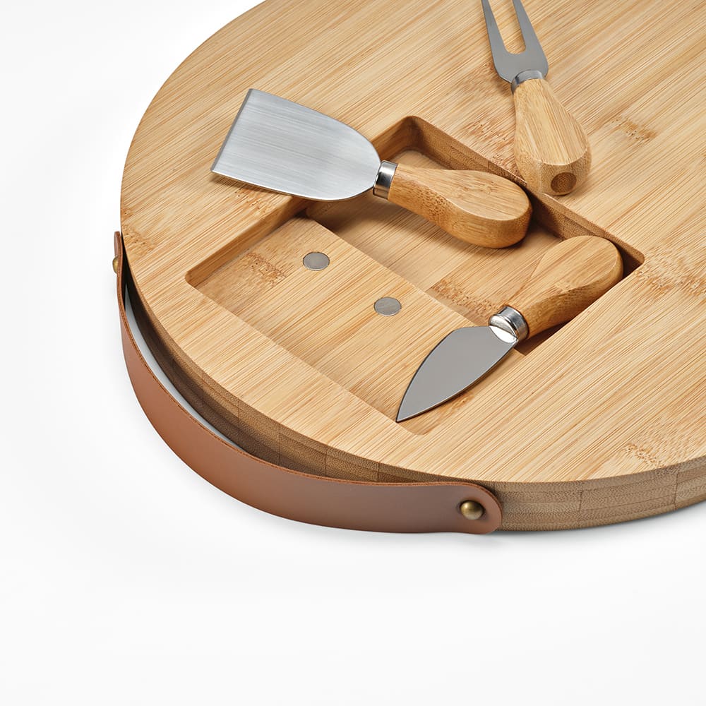 A bamboo cheese board with wooden-handled utensils, featuring a round design and a leather strap.