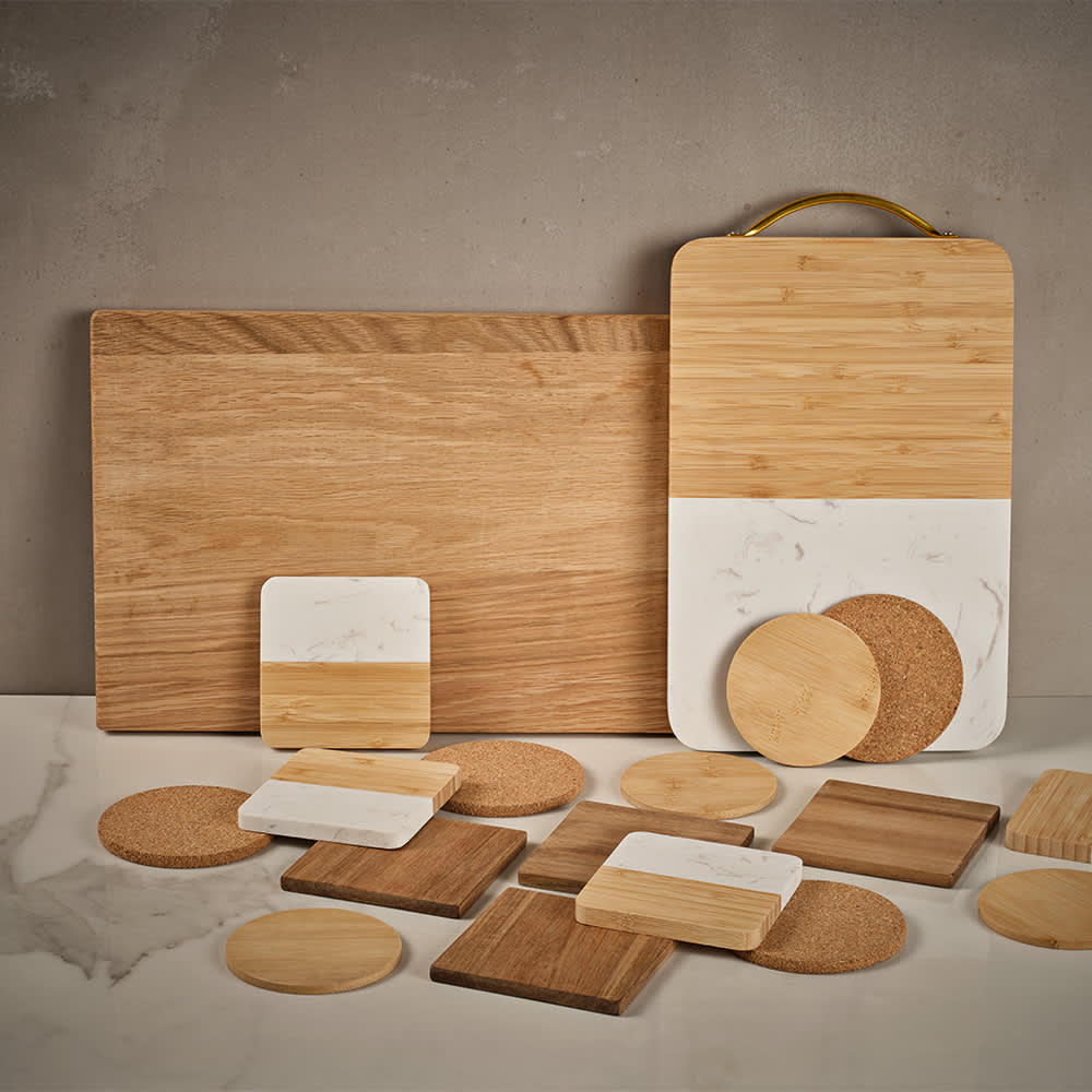 A wooden board with a built-in handle, featuring white marble, surrounded by various wooden and cork coasters.