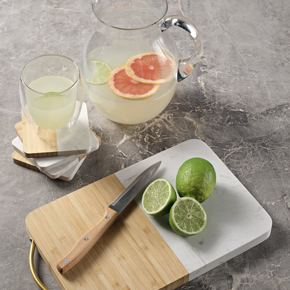 A marble and bamboo cutting board with a wooden handle, featuring freshly cut limes and a knife.