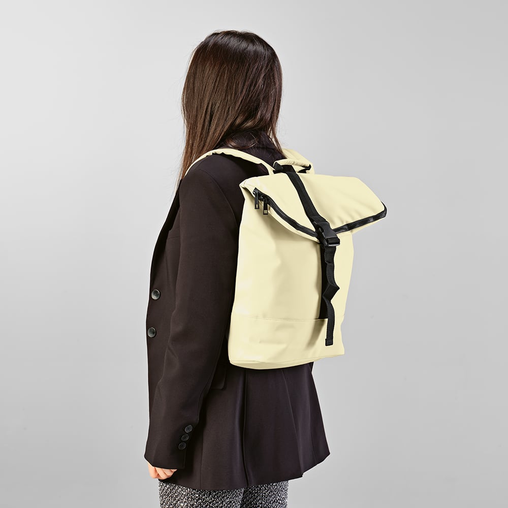 A yellow Milan Backpack with a roll-top design, featuring a black strap, worn by a person in a dark coat.