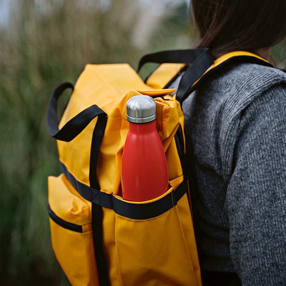 A yellow backpack with black accents featuring a red drink bottle in its side pocket.