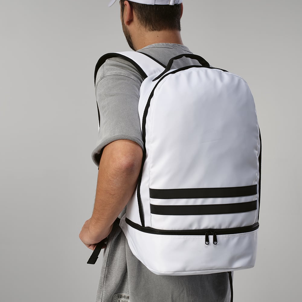 A white backpack with reflective front strips, worn on the back, featuring a logo on the front.
