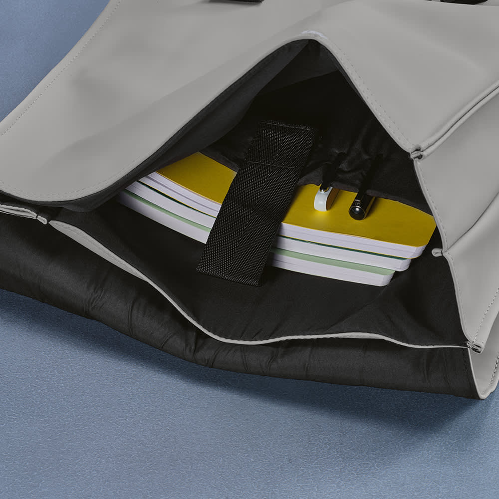 A grey backpack with a black interior, featuring compartments for notebooks and other items. It has a logo.