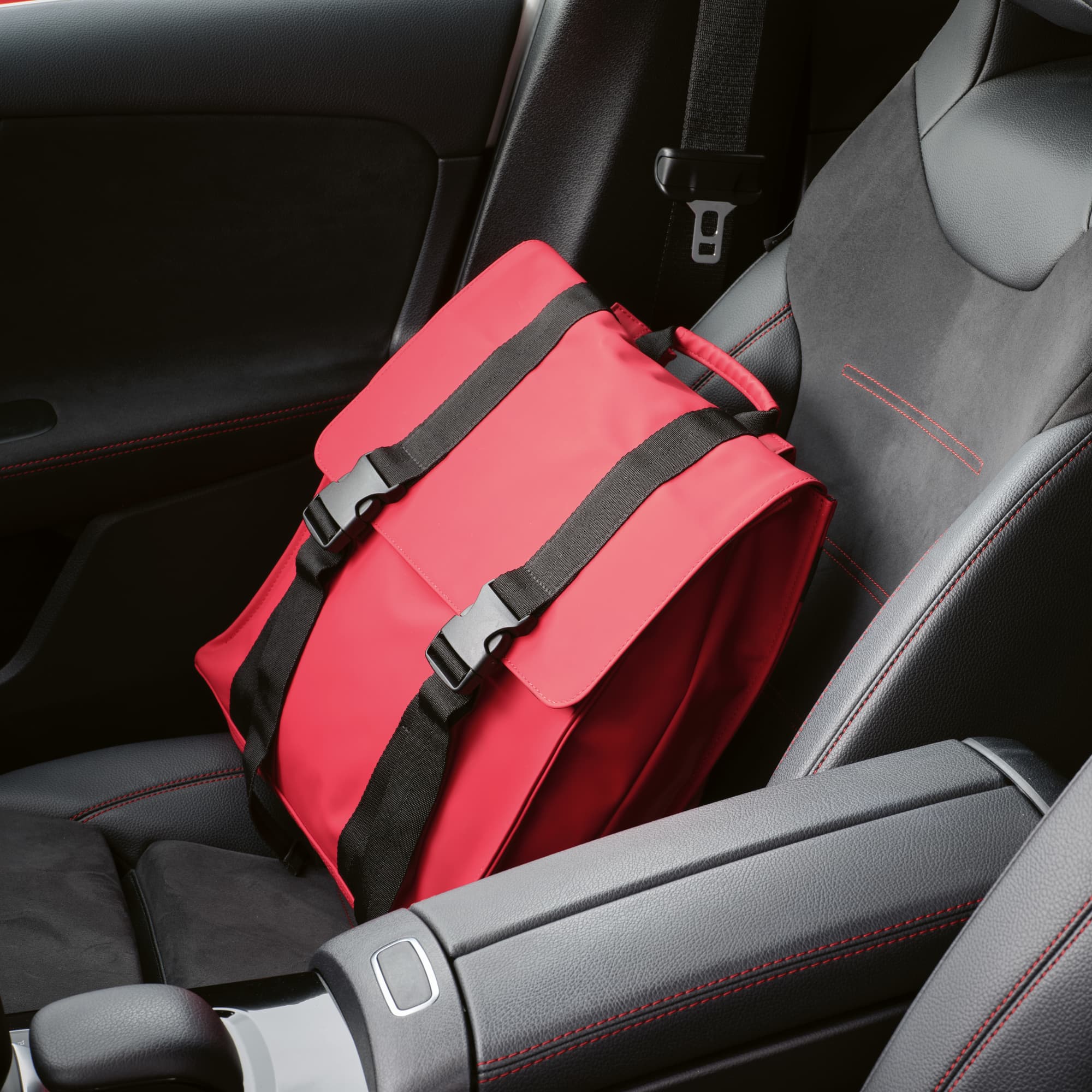 A red Edinburgh backpack with black straps rests on a car seat, showcasing its spacious design.