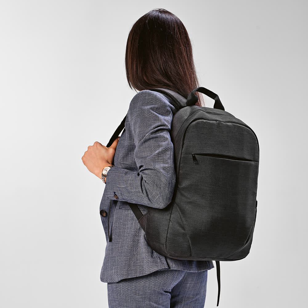 A black backpack with a front pocket, designed to fit a 17" laptop, worn on the back of a person in a suit.
