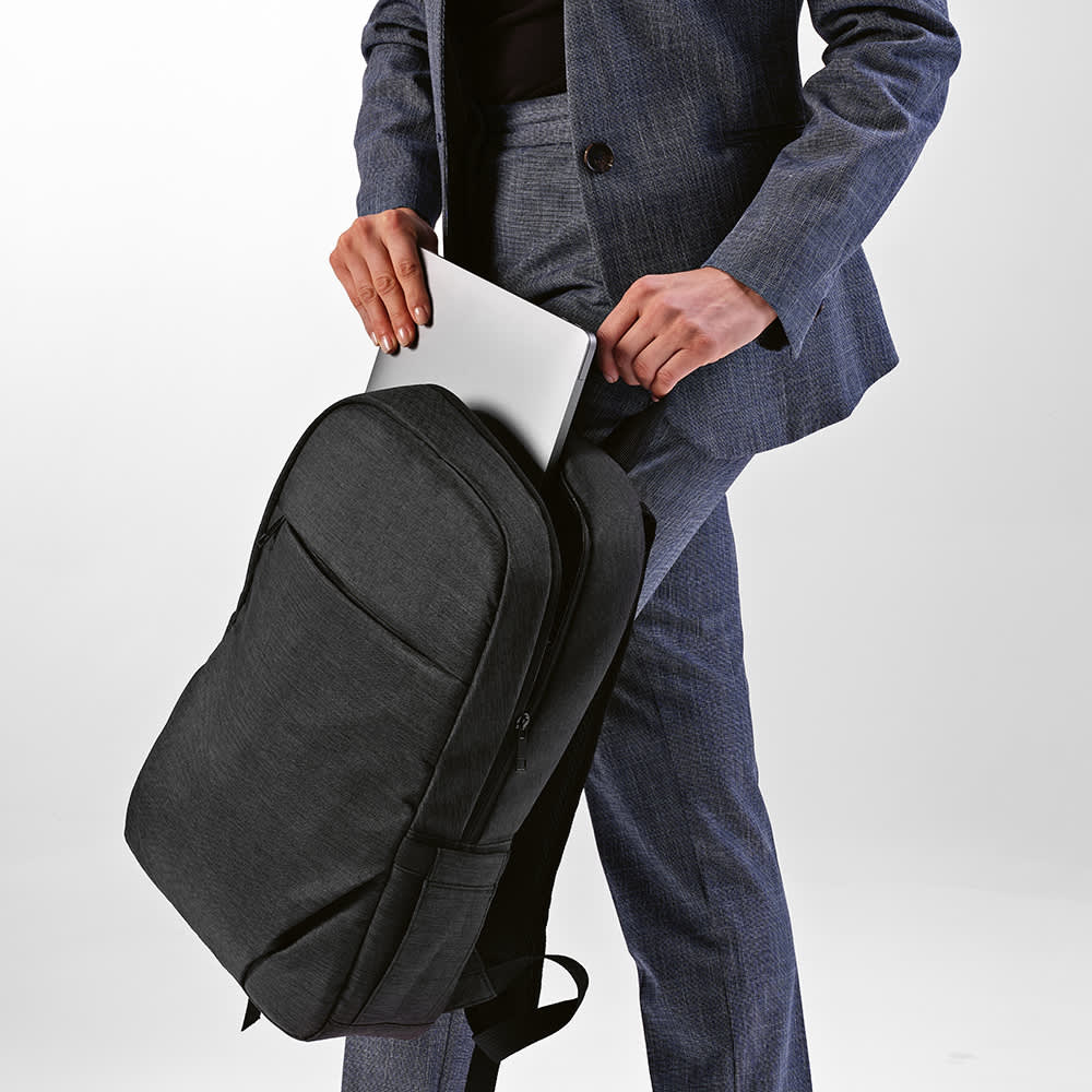 A black backpack with a front pocket, designed to fit a 17" laptop, being held by a person in a suit.