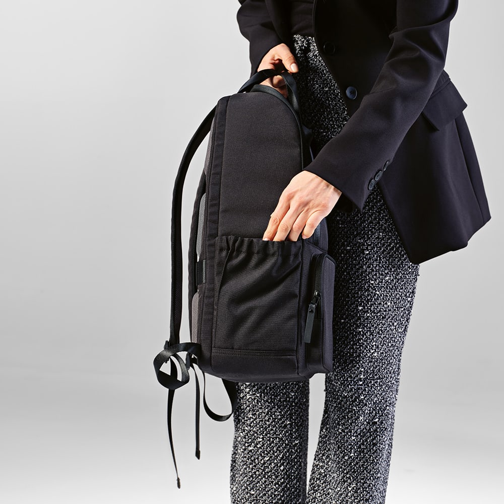 A black Bucharest backpack with a front pocket, designed to fit a 15.6" laptop, held by a person in formal attire.