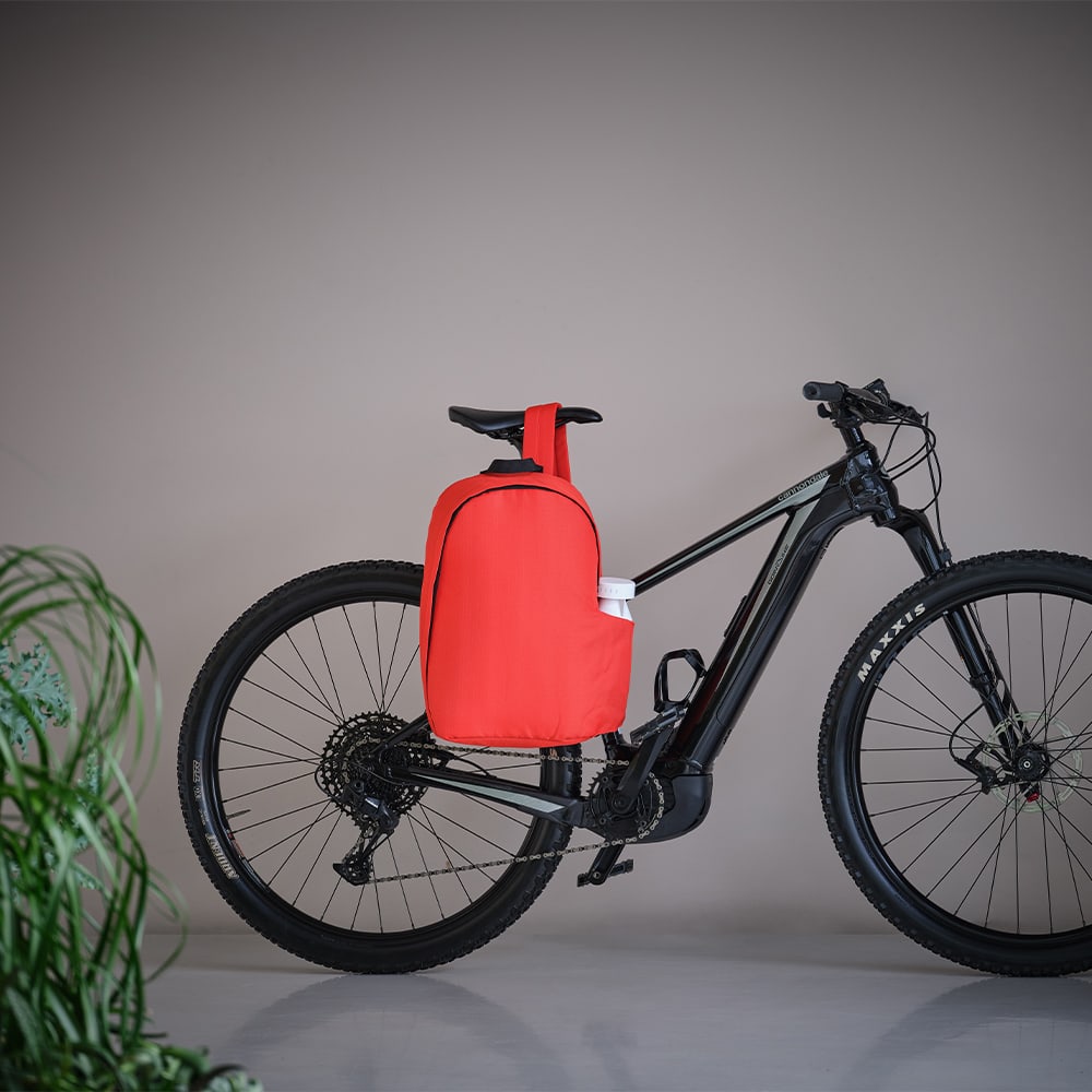 A red Tallin backpack with a logo, positioned on a black mountain bike against a neutral background.