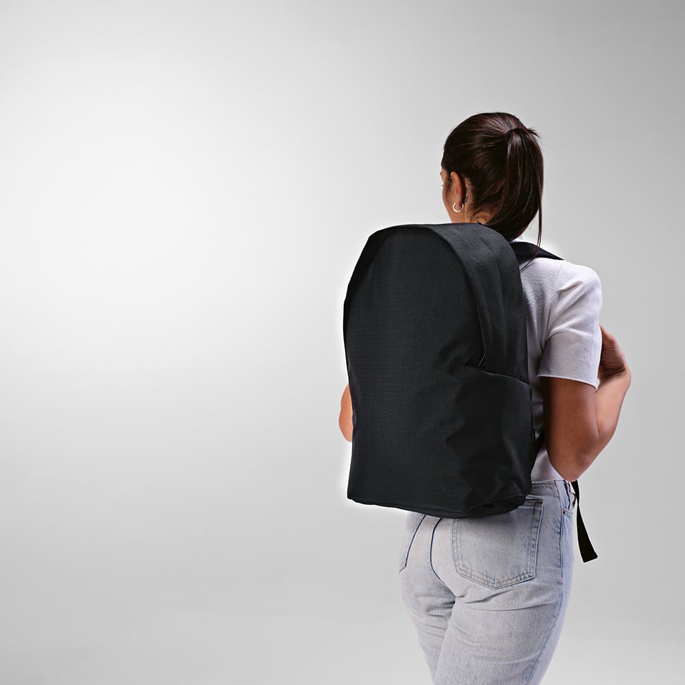 A black backpack with a sleek design, featuring adjustable straps, worn on a person’s back.