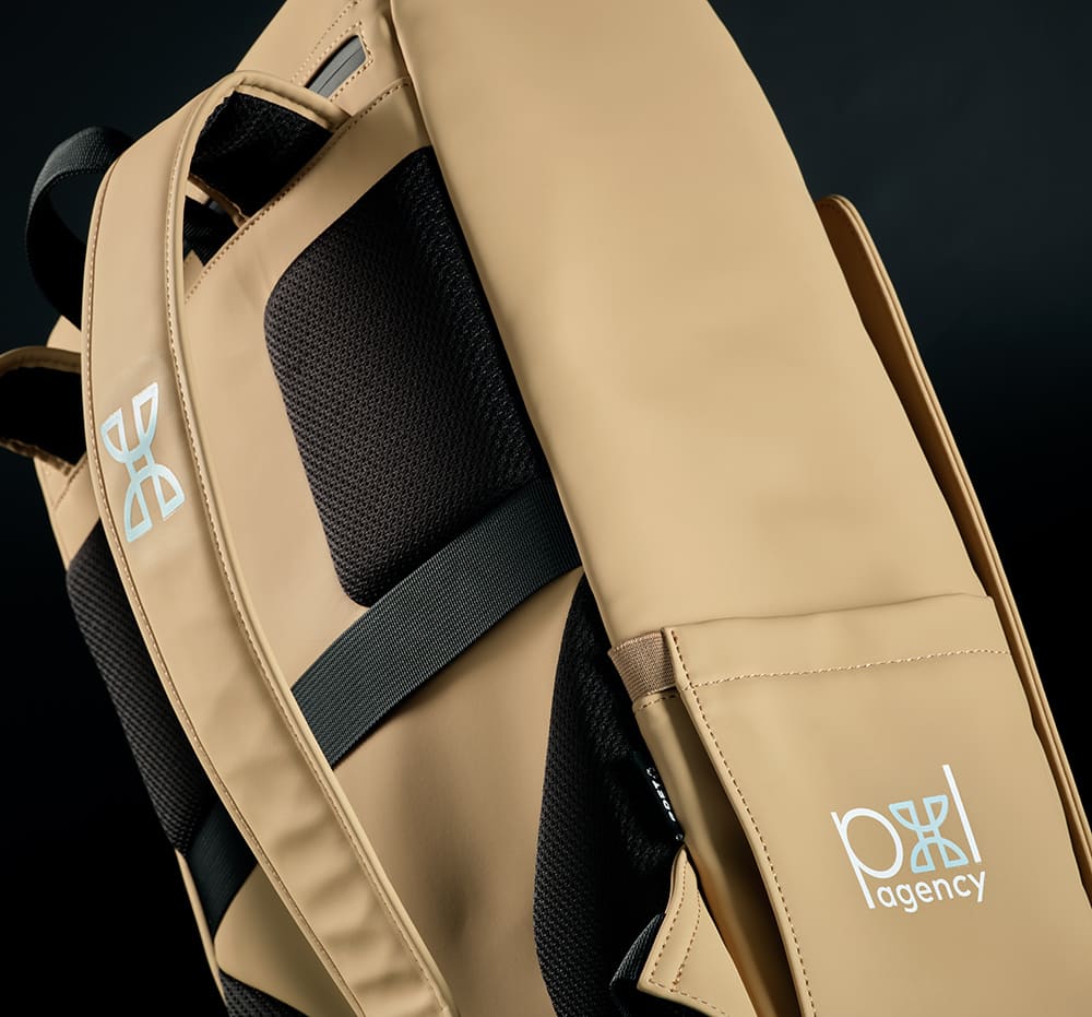 A tan backpack with a sleek design, featuring padded straps, mesh panels, and a logo on the side.