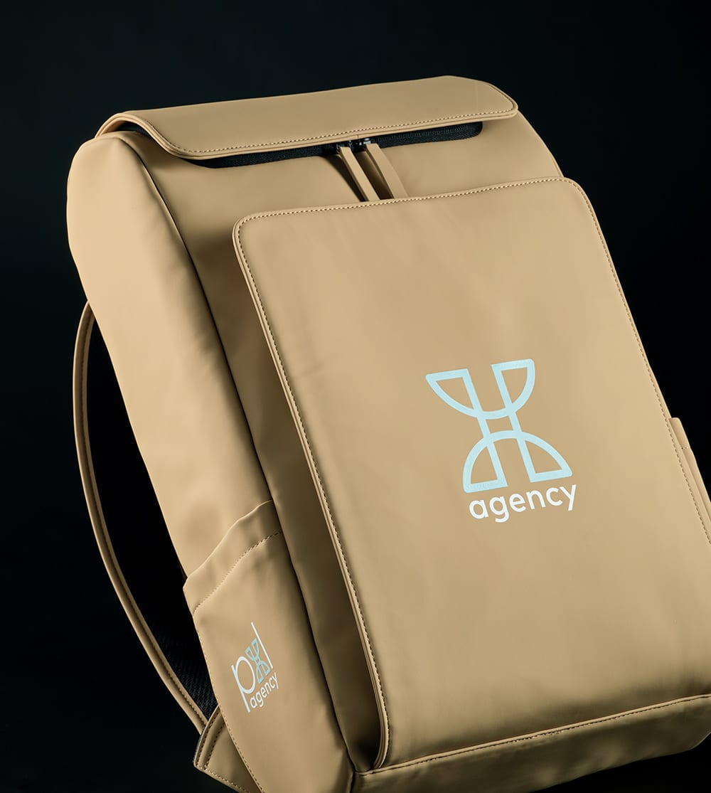 A tan backpack with a front pocket and logo, designed to fit a 15.6" laptop, with adjustable straps.