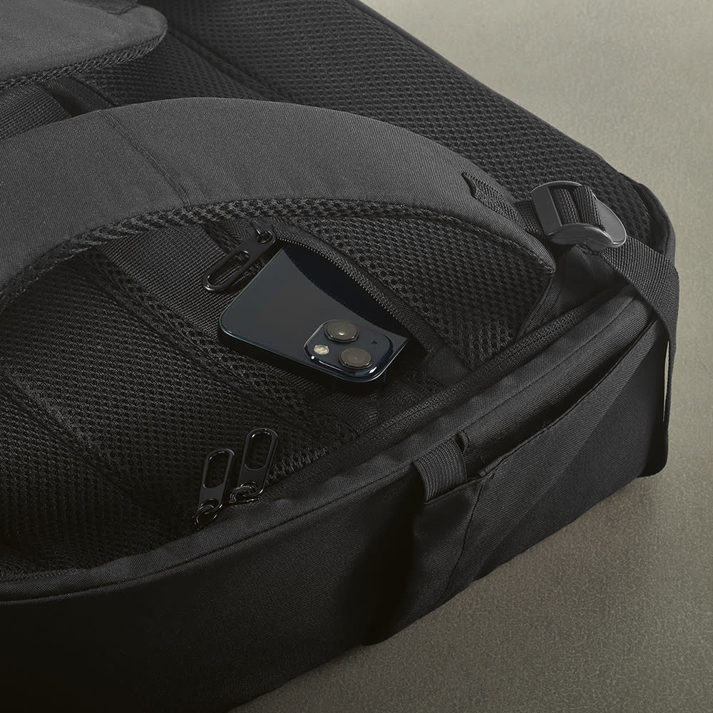 A black backpack with a front pocket, featuring a mesh compartment and a phone nestled inside.