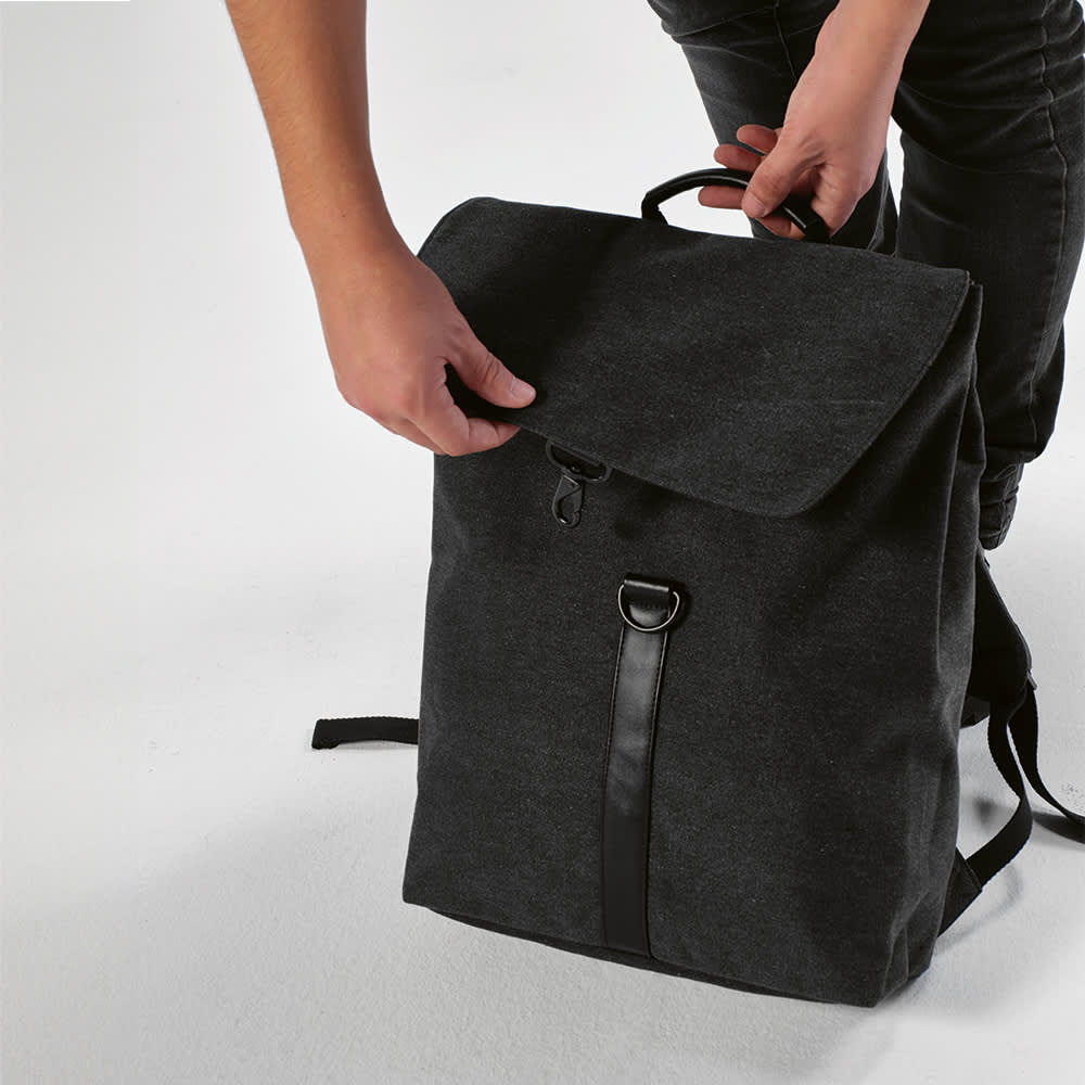 A black backpack with a hook closure and a handle, suitable for a 17" laptop, being opened by a person.