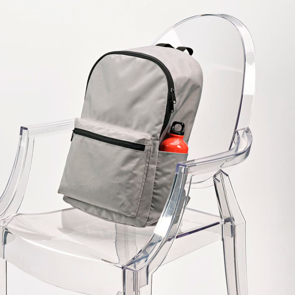A grey backpack with a front pocket and a drink bottle holder sits on a transparent chair. It has a logo displayed.