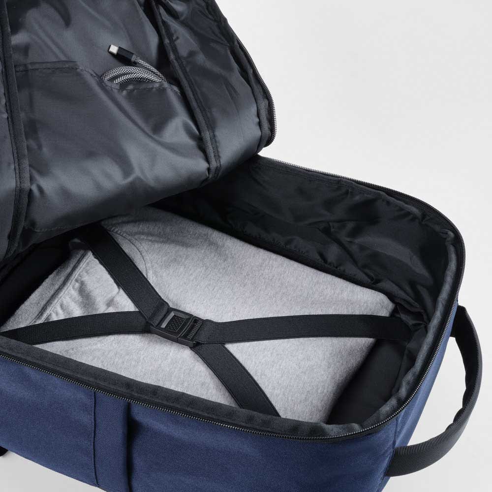 A navy blue backpack opened to reveal a grey sweatshirt secured inside with straps, featuring an interior pocket.