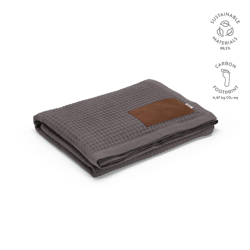 A grey Giotto blanket made from sustainable materials, featuring a customisable brown patch. It has a textured design.