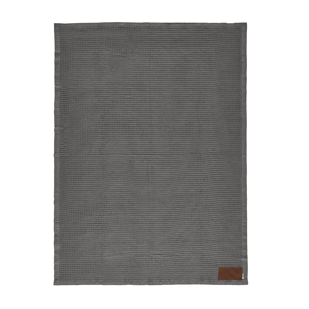 A grey blanket with a textured pattern and a brown patch featuring branding. Ideal for customization.
