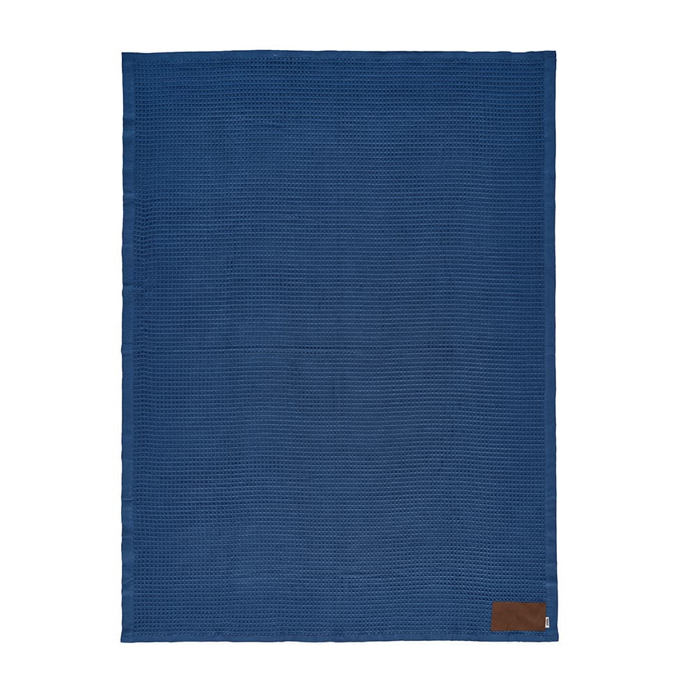 A blue blanket made of cotton, featuring a customisable patch and a branding logo at the bottom.