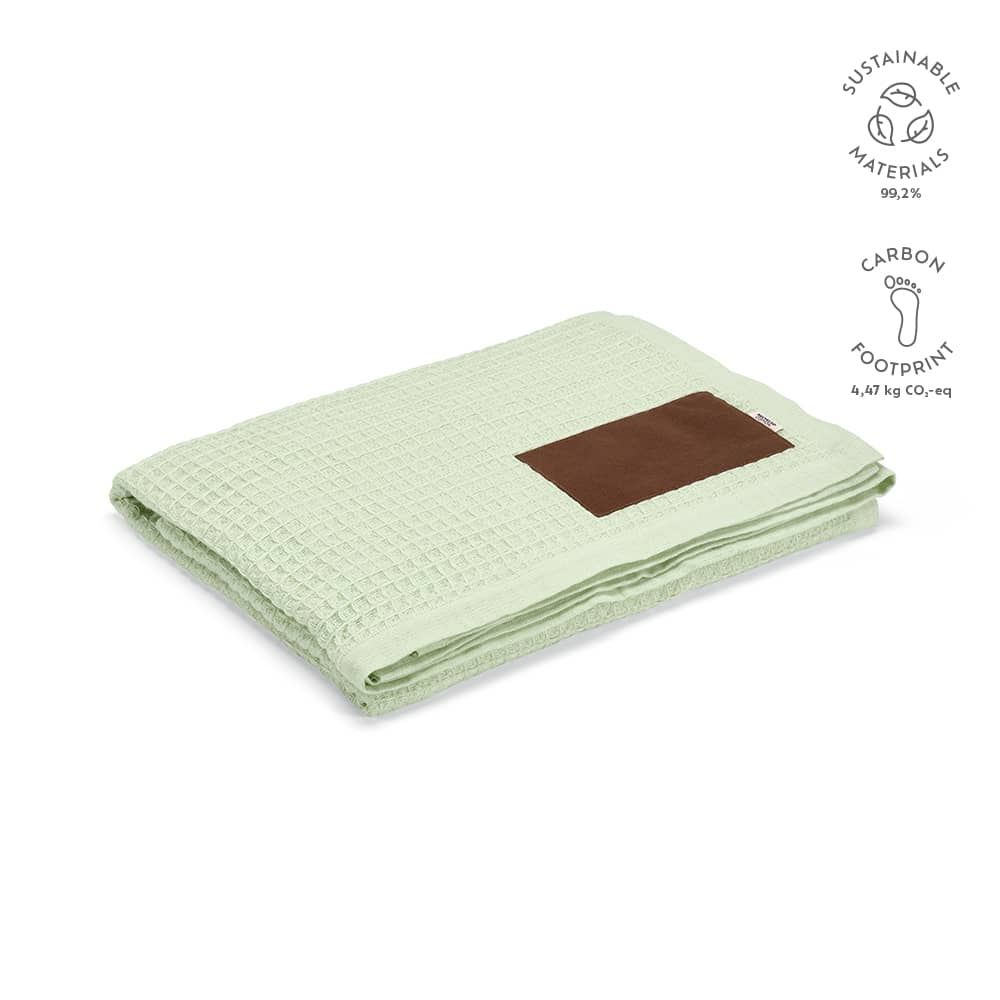 A light green Giotto blanket made of sustainable materials with a brown customizable patch.