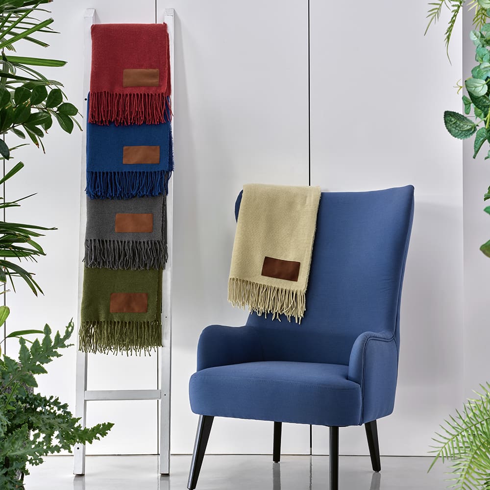 A stack of colourful Lichtenstein blankets in red, blue, green, grey, and beige displayed alongside a blue armchair.