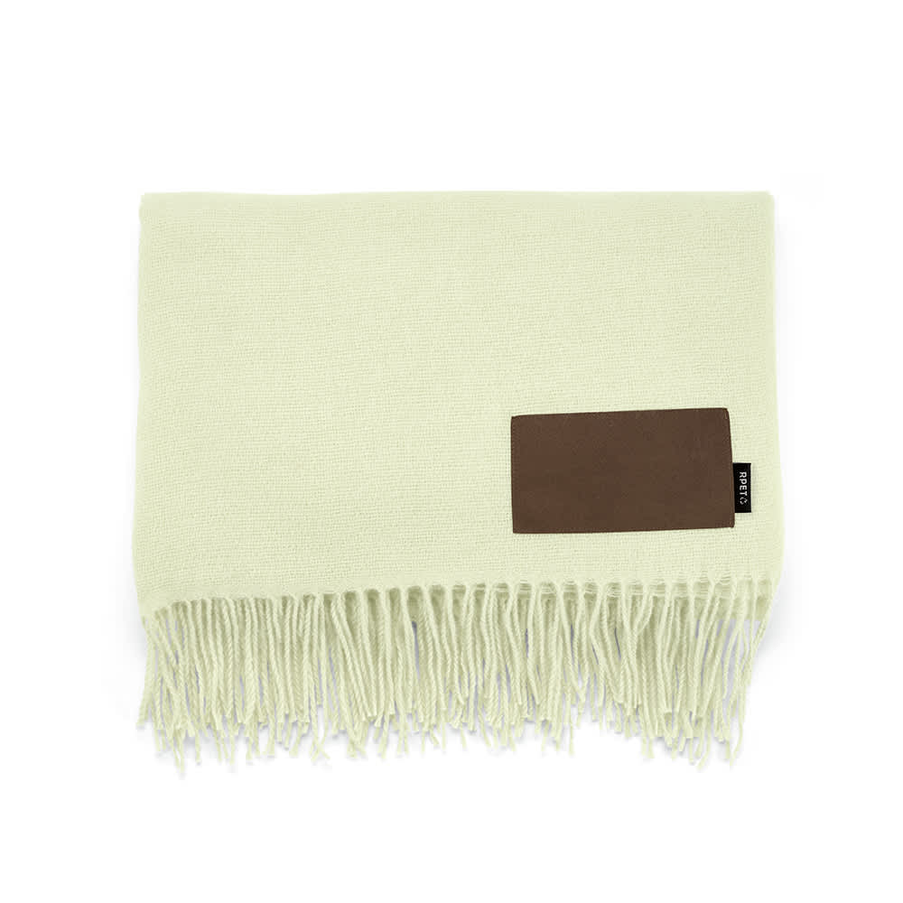 A light green blanket with fringes and a brown customisable patch. It features a logo on the patch.