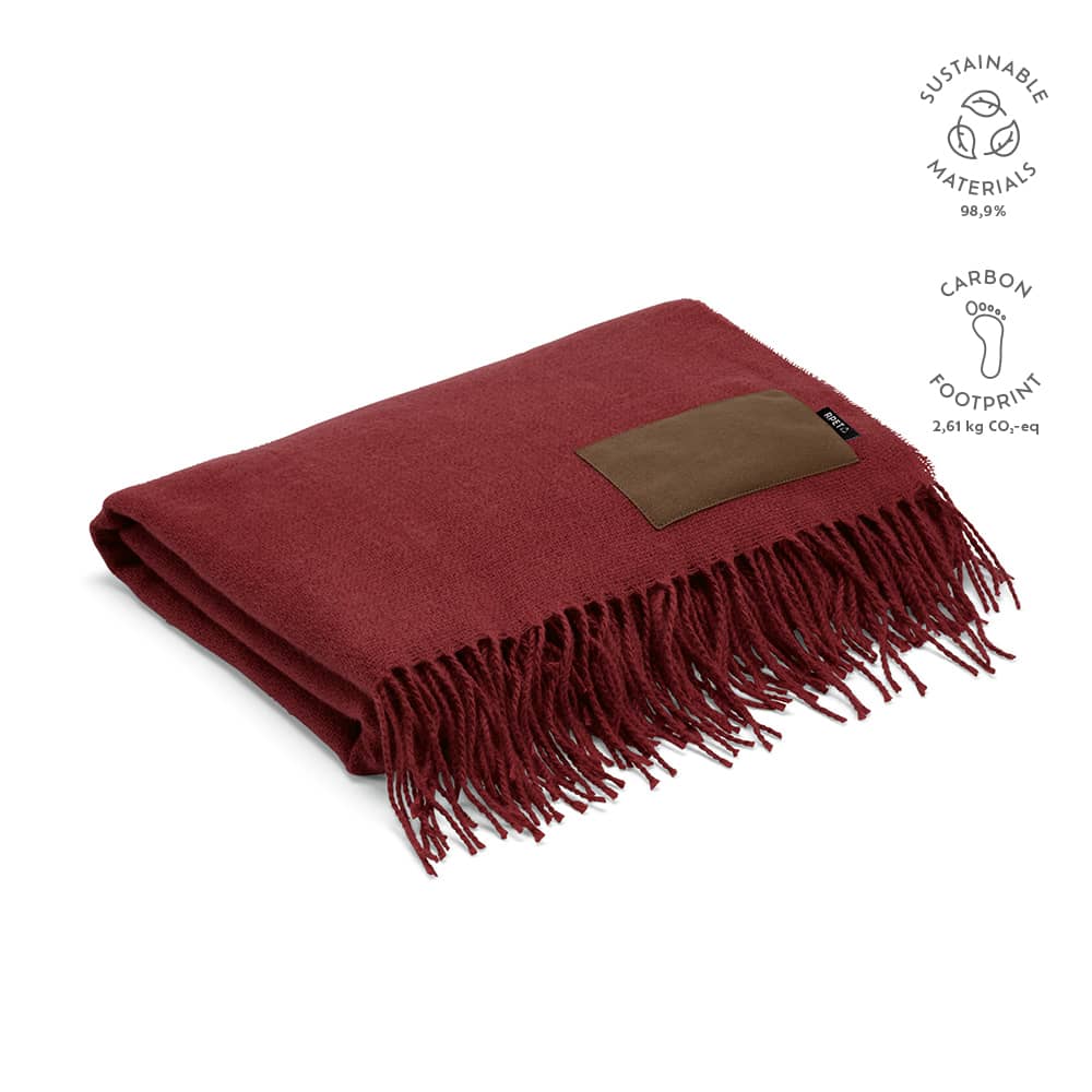 A maroon blanket with fringed edges and a brown customisable patch. Features sustainable materials.