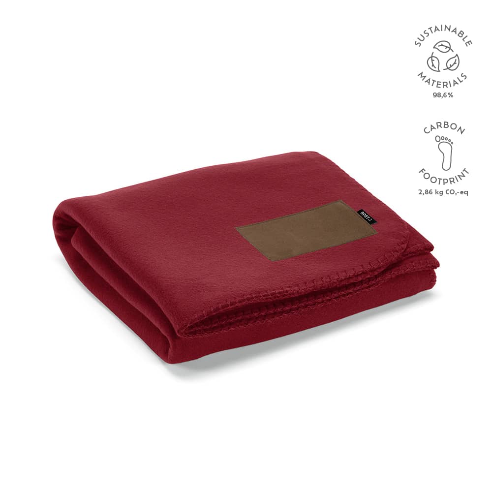 A red blanket made from sustainable materials, featuring a customisable patch area. It has a logo displayed on the side.