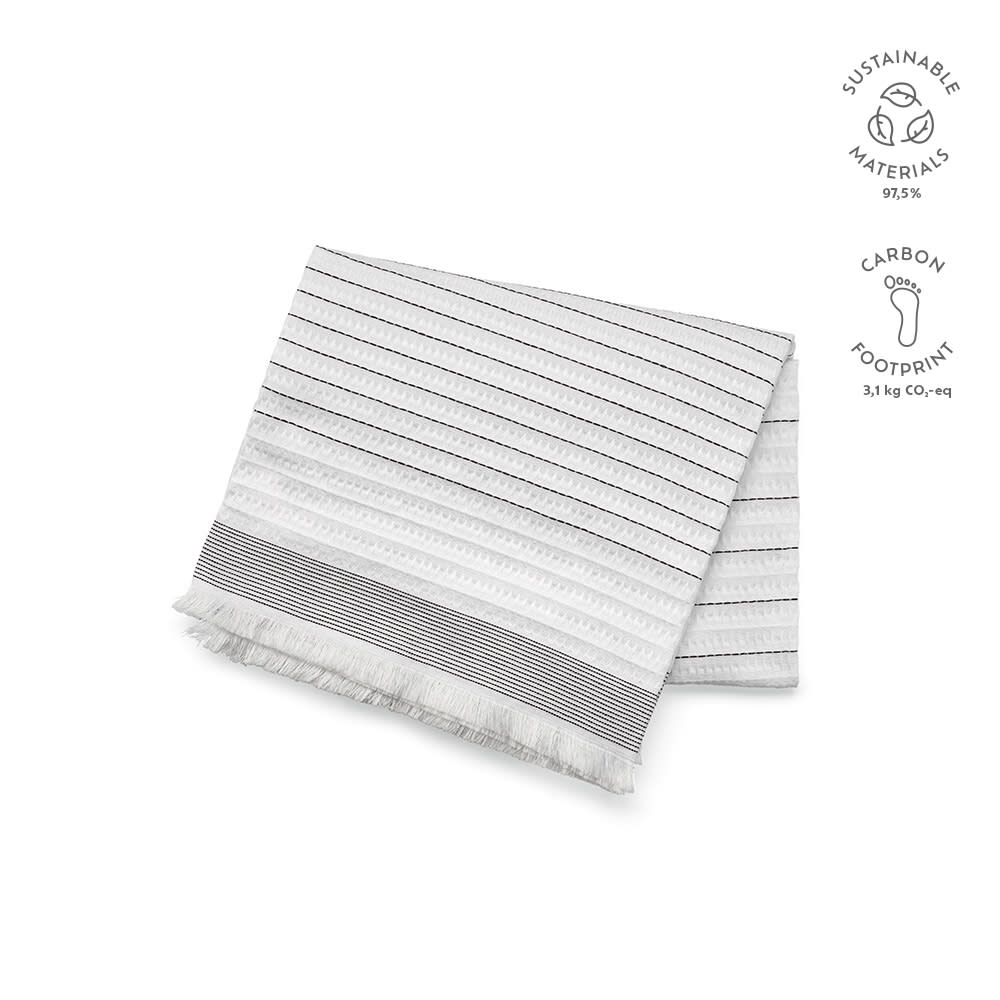A cotton blanket in white with black stripes and fringed edges, featuring sustainable materials branding.