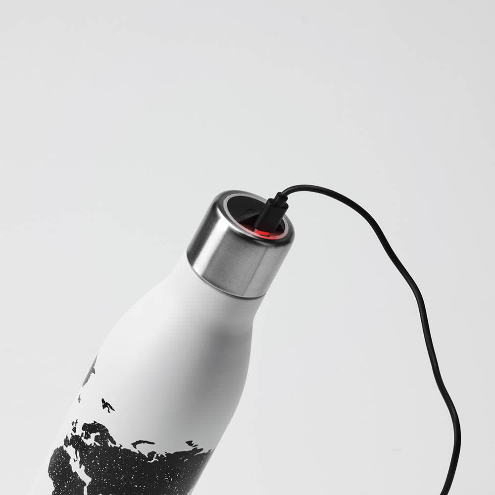 A drink bottle in white with a metallic lid, featuring a black design and a charging cable attached.
