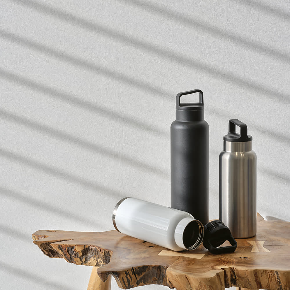 A drink bottle collection featuring a black bottle, a silver bottle, and a white bottle, all with various caps, on a wooden surface.