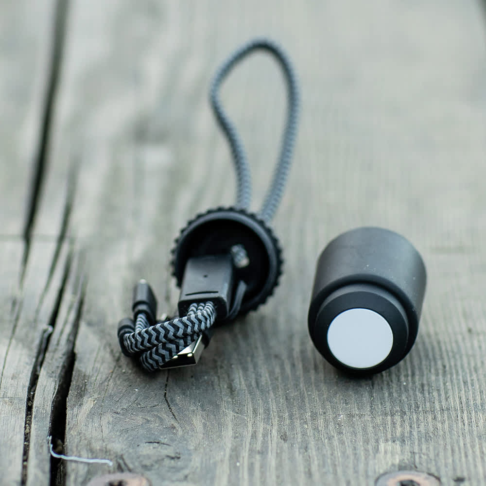 A black 5-in-1 charging cable with a textured grip and a looped cord. It has an attached connector and a round end.