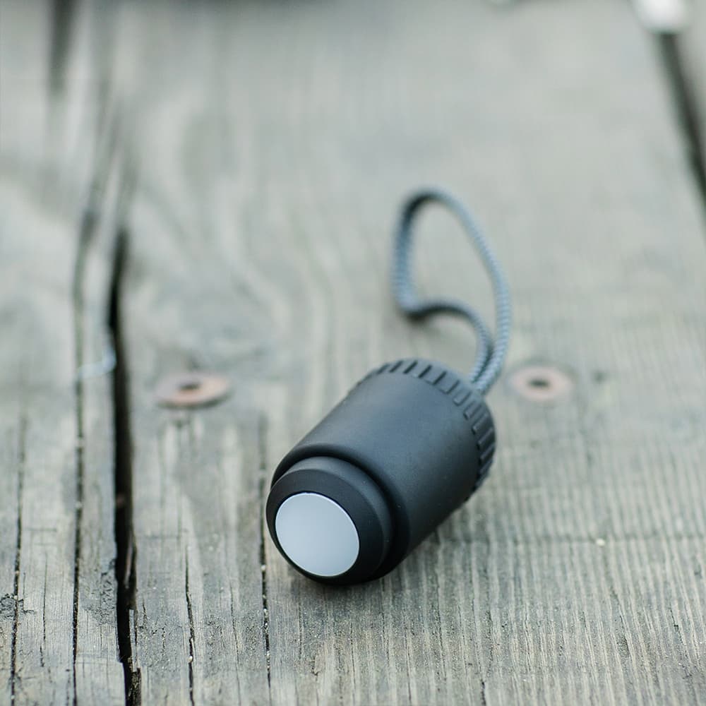 A black cable with a round connector and a looped attachment, resting on a wooden surface.