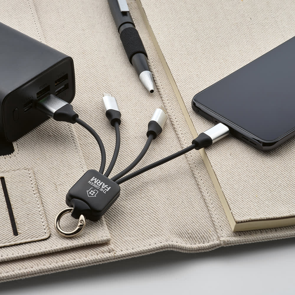 A 4-in-1 charging cable in black, featuring a keyring attachment and multiple connectors, resting beside a smartphone and power bank.